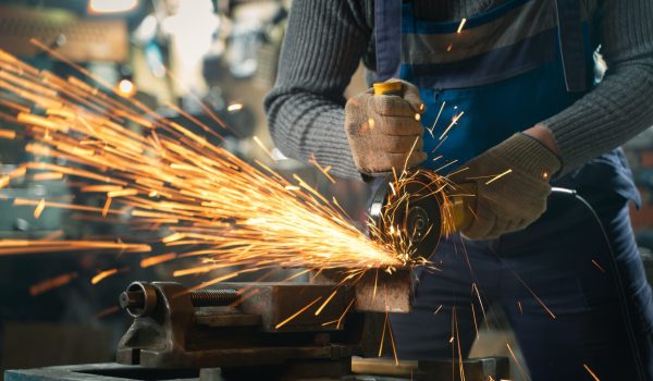 Locksmith in special clothes and goggles works in production. Metal processing with angle grinder. Sparks in metalworking.